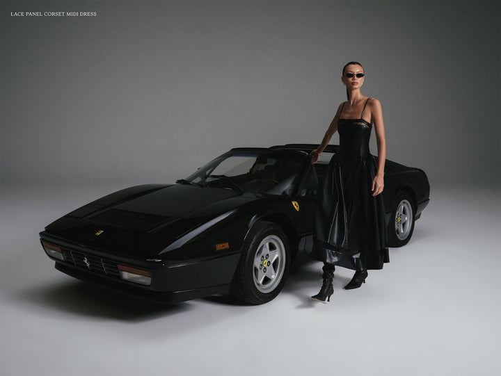 Woman in a black dress standing next to a black Ferrari car on a gray background