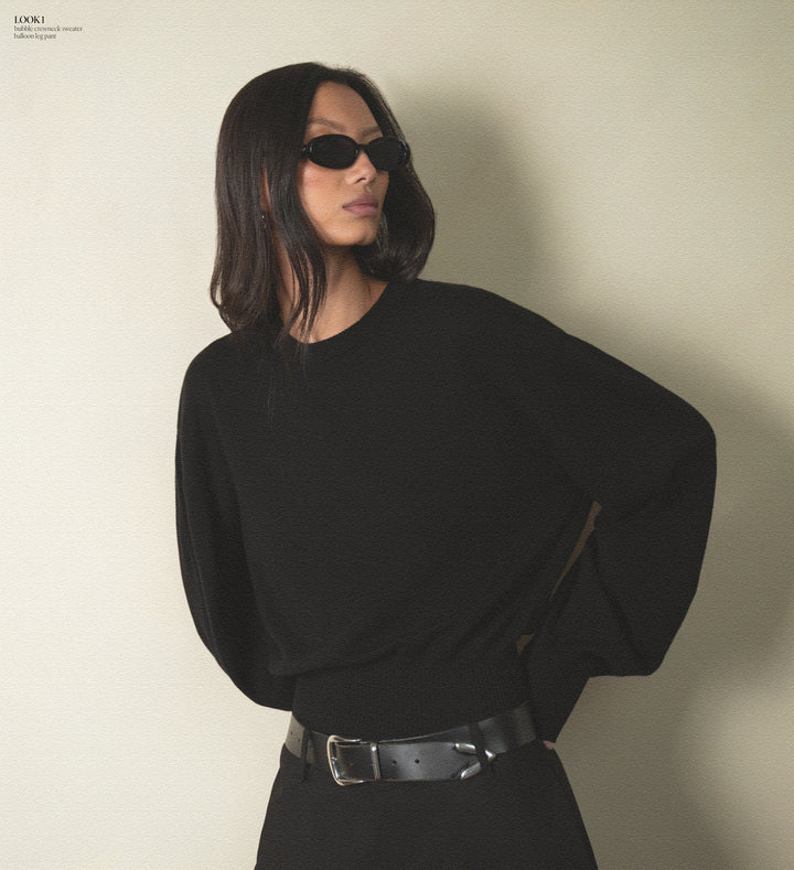 Person wearing a black outfit with sunglasses against a plain background