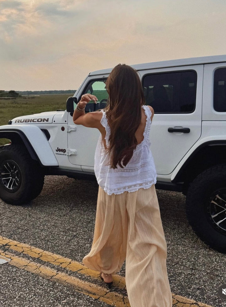 Woman taking a photo of a white Jeep Rubicon in a field at sunset.