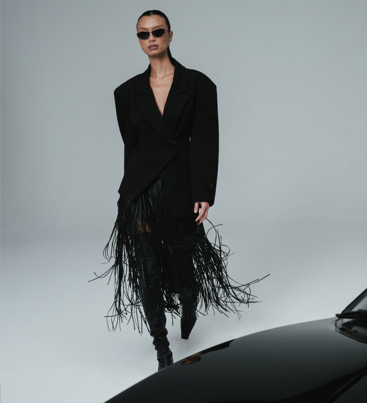 Person wearing a black fringe WeWoreWhat outfit with sunglasses on a gray background