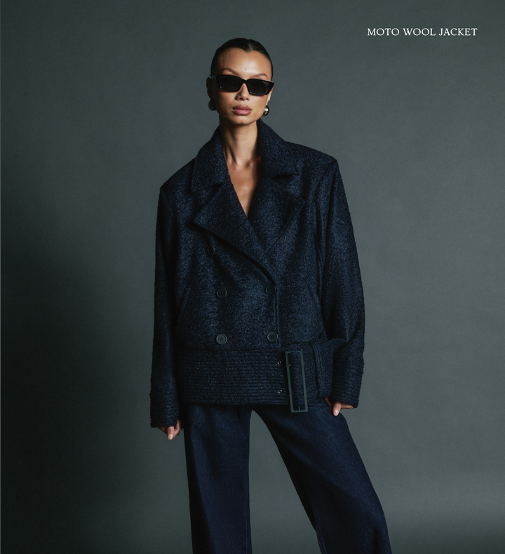 Person wearing a dark blue moto wool jacket on a gray background