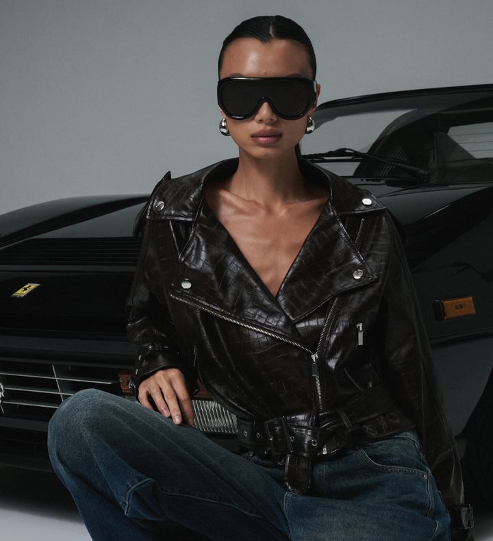 Person wearing a black leather jacket and sunglasses in front of a black car