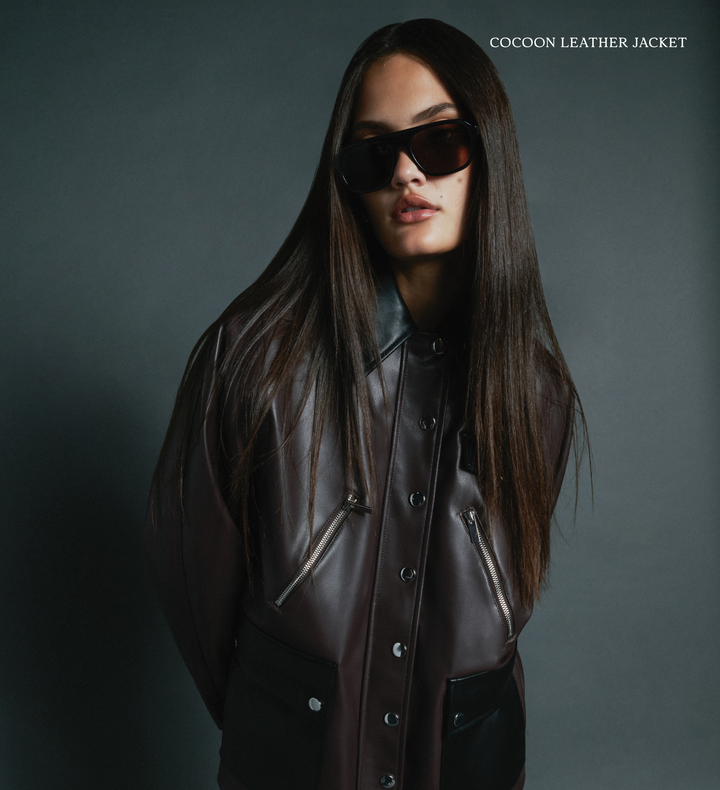 Person wearing a brown leather jacket and sunglasses on a dark background