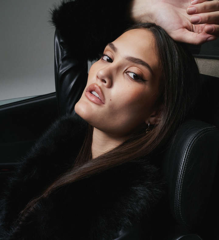 Woman sitting in a car wearing a black fur coat with a blurred background